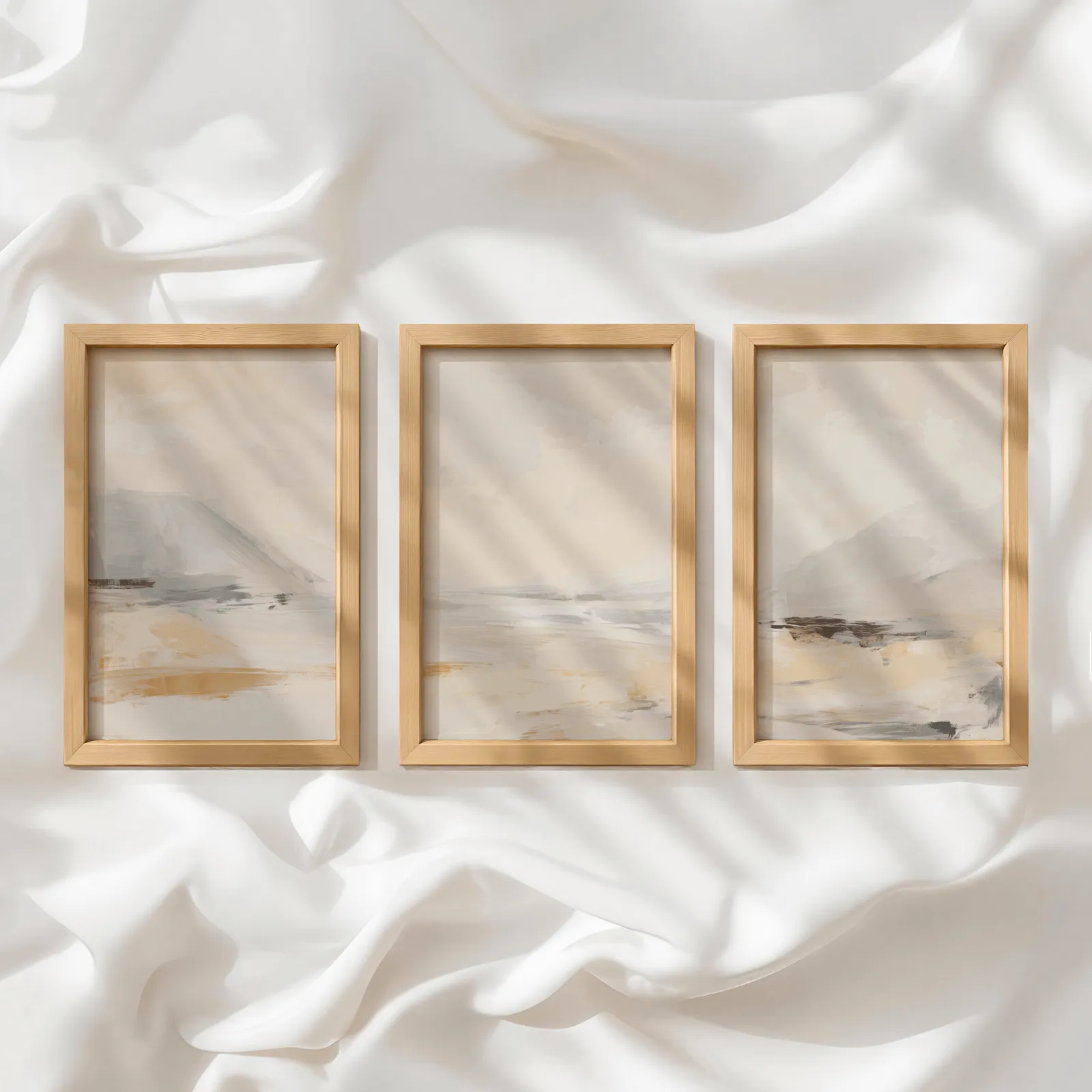 beige abstract landscape wall art set of three, in a row atop rumpled white silky fabric