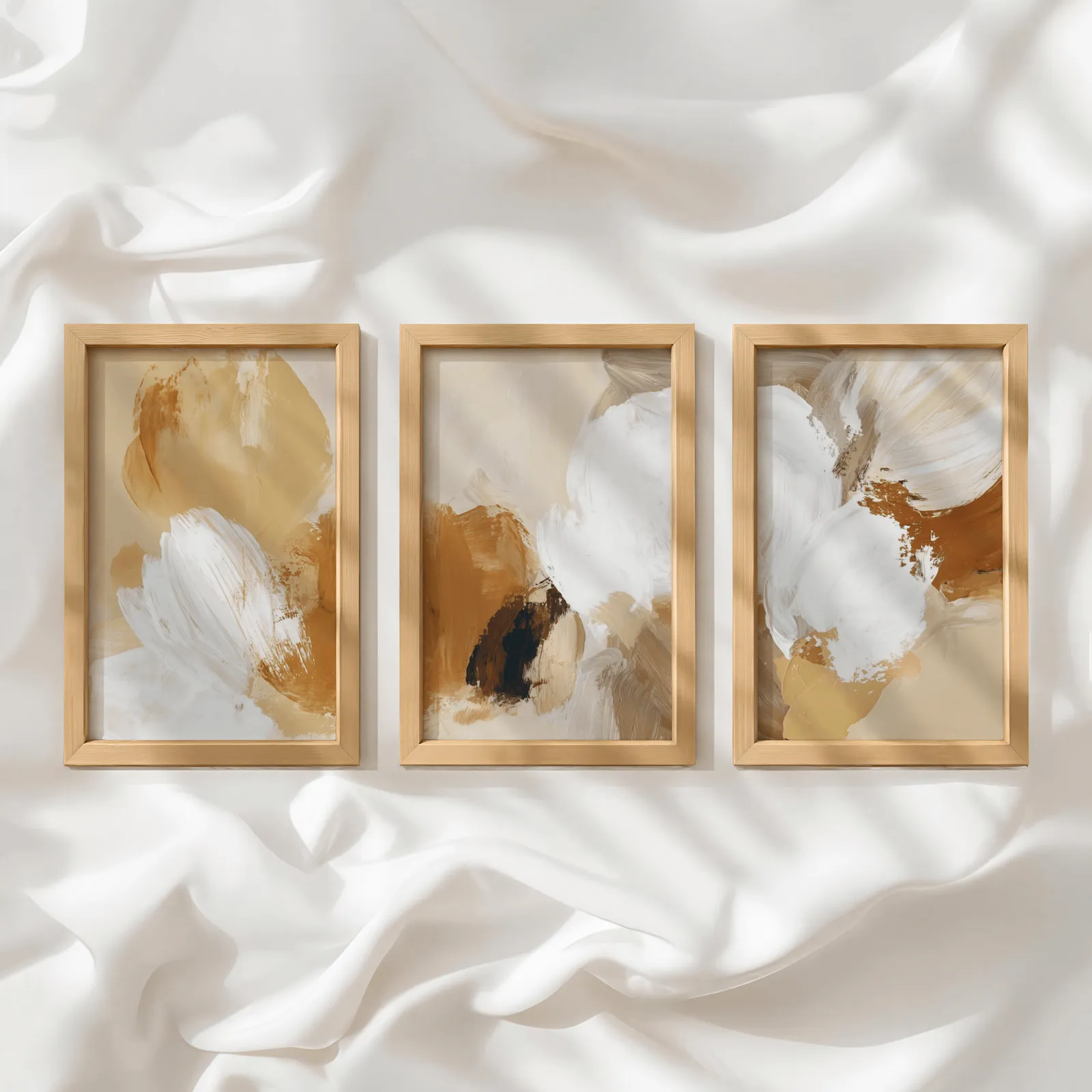 beige abstract triptych wall art set of 3, in a row atop rumpled white silky fabric